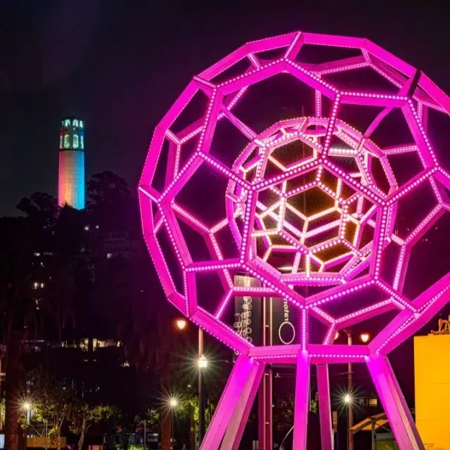 Buckyball brilla fuera del Exploratorium, con la Torre Coit al fondo